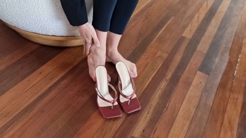 Ženski par stopala ispred crvenih japanki na štiklu sa kvadratnim vrhom, na drvenom podu.