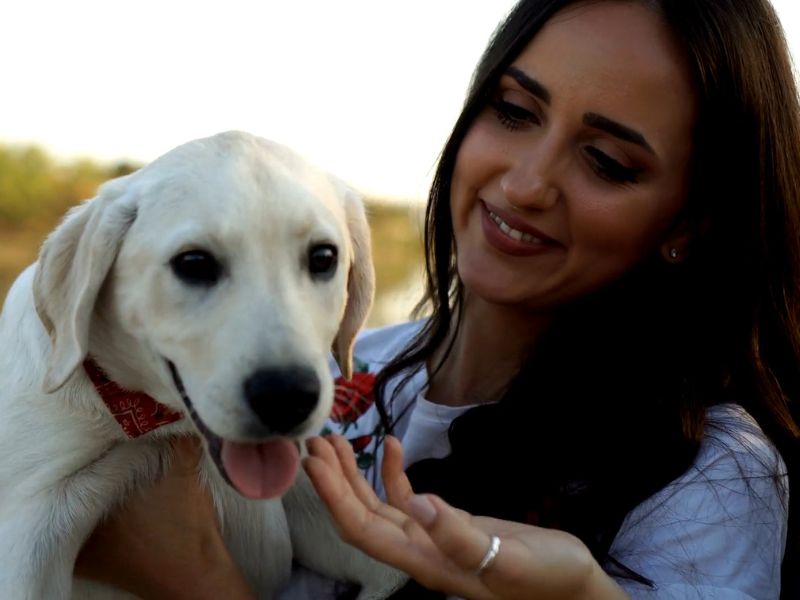 Devojka crne kose se smeši dok drži svog psa u rukama